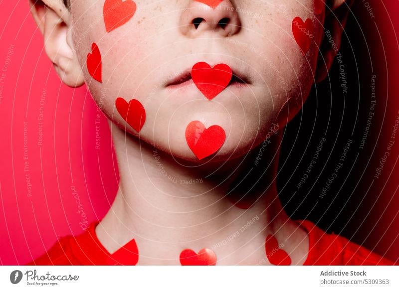 Anonymous cute boy in red casual shirt with red love sticker on face while posing for photograph kid studio modern adorable child childhood little colorful