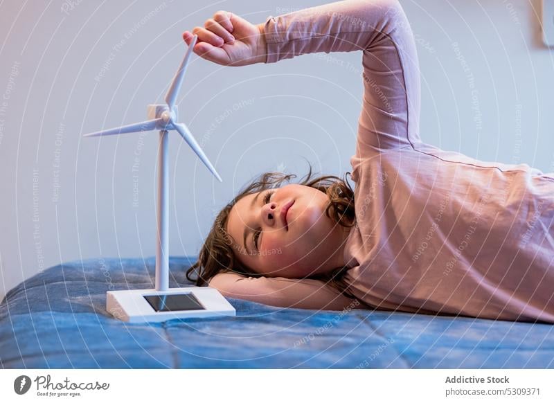 Girl playing with mockup of wind turbine on bed girl kid child having fun bedroom childhood happy smile joy positive lying comfort home dream cute soft adorable