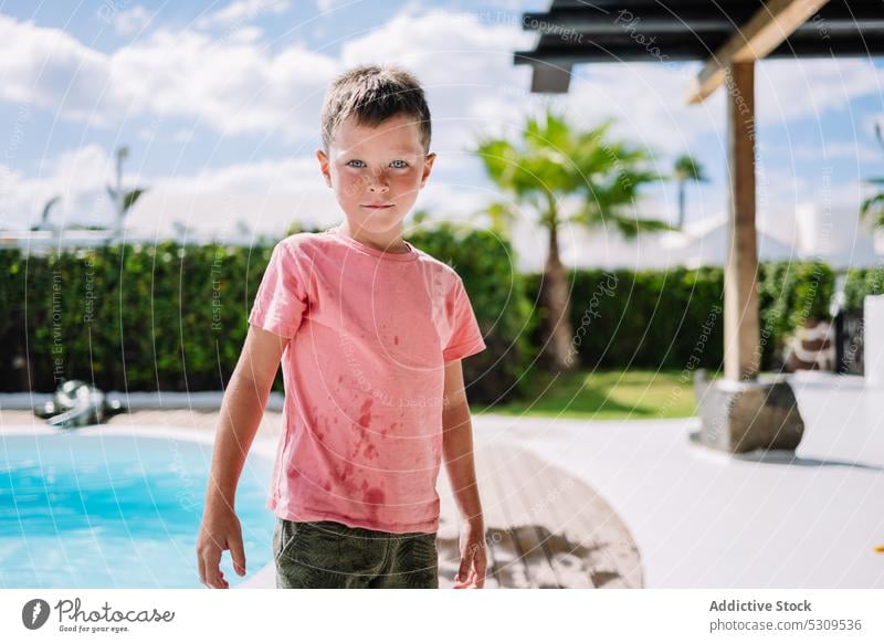 Cute boy in wet clothes near pool looking at camera summer poolside resort holiday vacation child kid rest water childhood adorable cute swim weekend sun