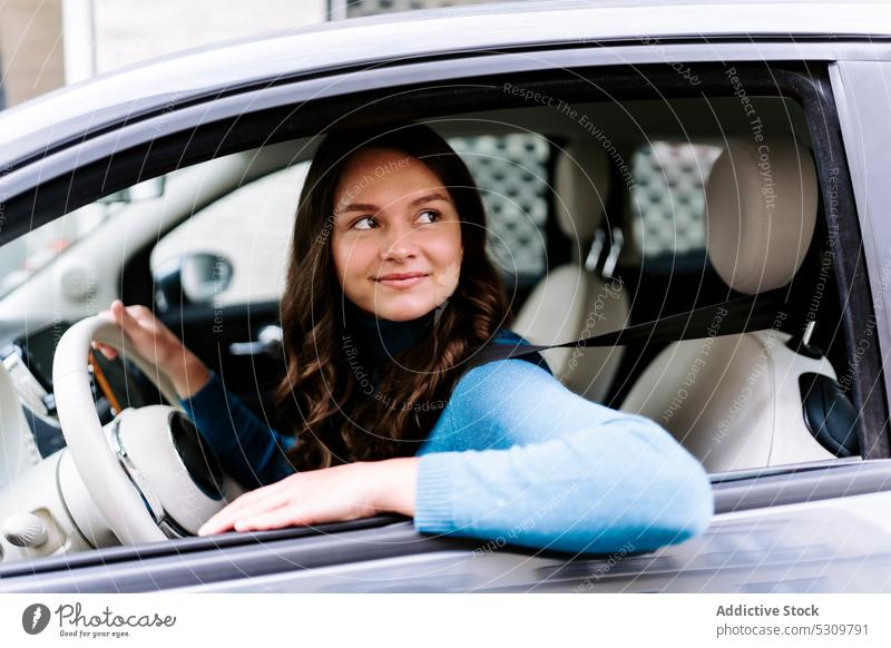 Positive woman sitting at car wheel smile happy driver automobile vehicle steering wheel transport trip young blouse female stripe white modern positive joy