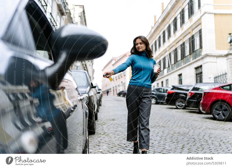 Young woman locking car with electronic key positive automobile city street vehicle coffee takeaway hot drink female young long hair to go modern urban beverage