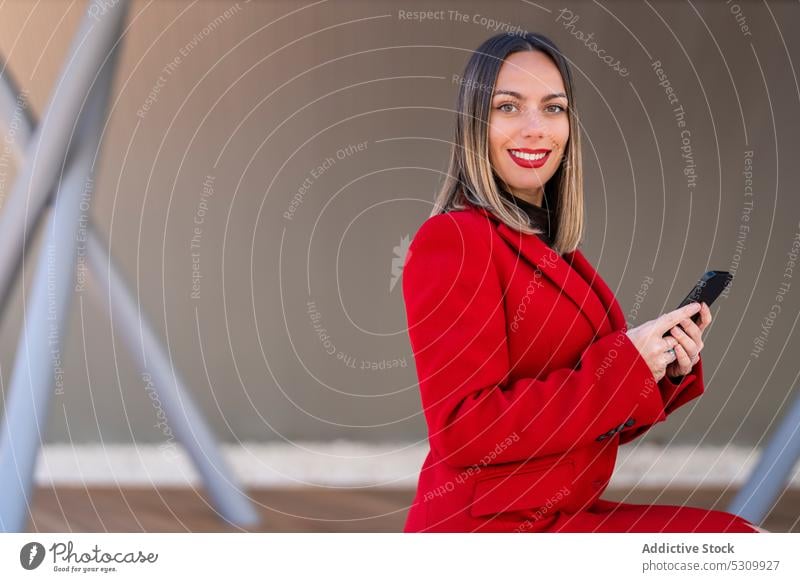 Smiling female with smartphone on street woman smile happy sit looking away cheerful device mobile young red lipstick cellphone lady glad positive lifestyle joy