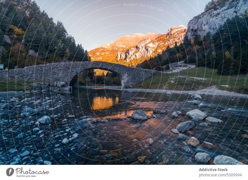 Old stone bridge over calm river in nature mountain lake sunset shore sundown landscape highland picturesque pyrenees fall autumn national park evening water