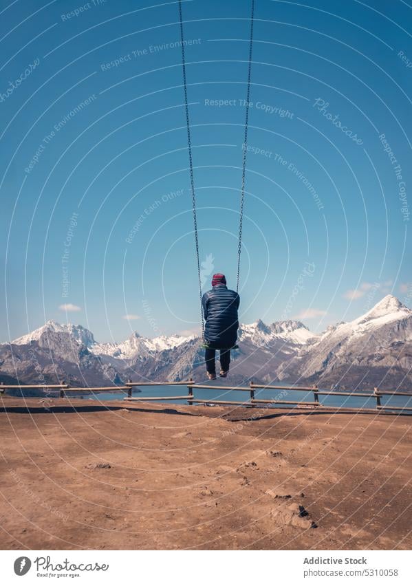 Unrecognizable traveler swinging on rope in sandy terrain by mountains and river man hang vacation nature tourism blue sky tourist spain calm riano casual cozy