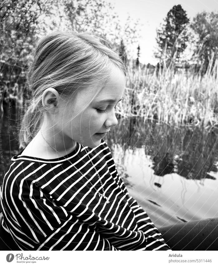 Girl sitting in boat with lake and shore in background looking down b/w Lake Pedalo Child Water bank Head striped shirt Leisure and hobbies Trip Exterior shot