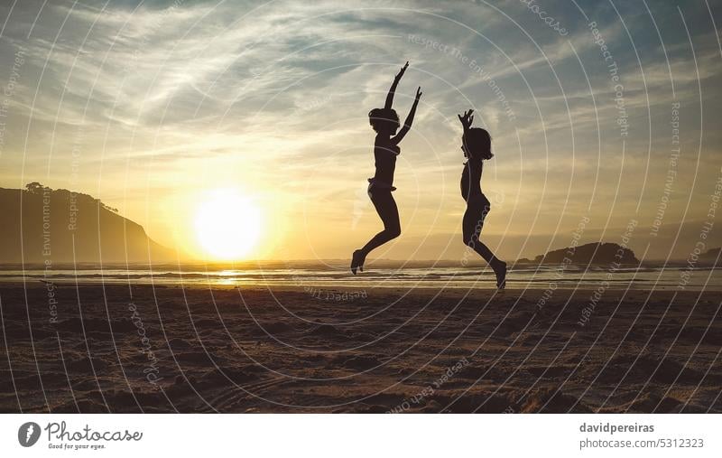 Silhouettes of two little girls jumping in the beach at sunset child friend silhouette playing unrecognizable sunrise sand happiness happy fun young freedom