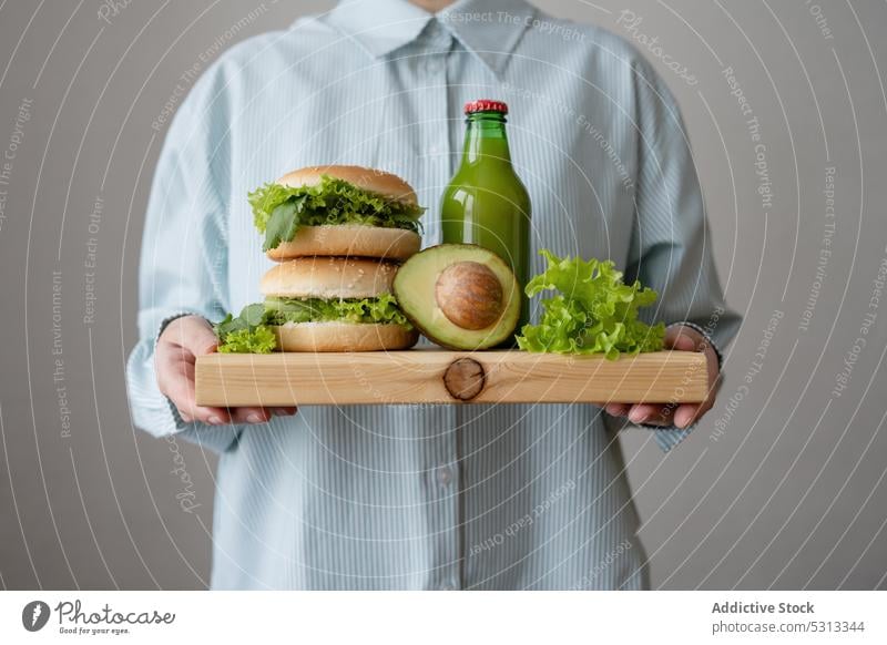 Crop cook with vegan burgers on wooden cutting board lettuce hamburger vegetarian avocado bottle juice drink refreshment green tasty meal bun woman lunch food