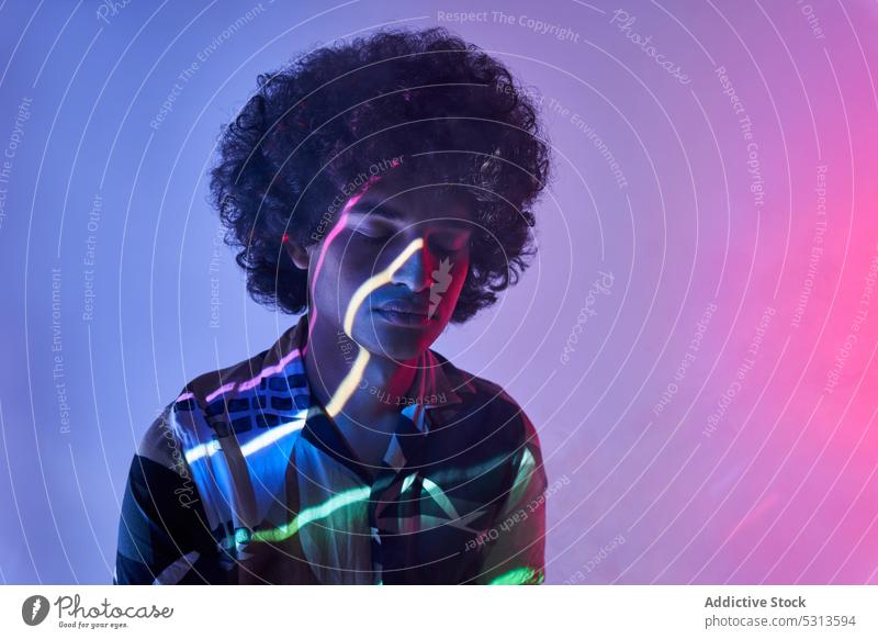 Hispanic guy against colorful illumination looking at camera man model multicolored afro hair illuminate projector glow creative portrait studio shot