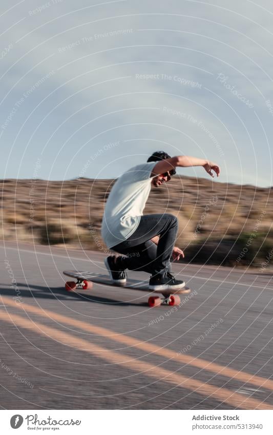 Carefree man balancing on skateboard on asphalt road trick skater ride extreme adrenalin balance activity energy male motion perform hill fast hobby speed skill