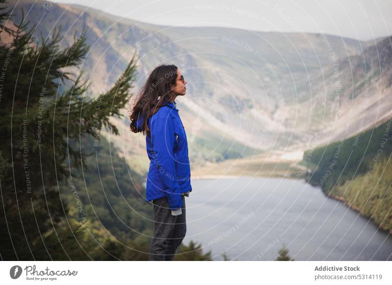 Young woman standing on mountain top and admiring view traveler lake hill nature admire coniferous water ireland scenery landscape picturesque tree female