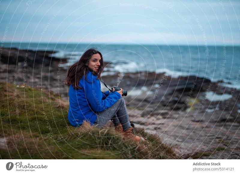 Young woman with professional camera sitting on seashore tourist photo camera coast nature ocean smile vacation ireland traveler photographer sunset female