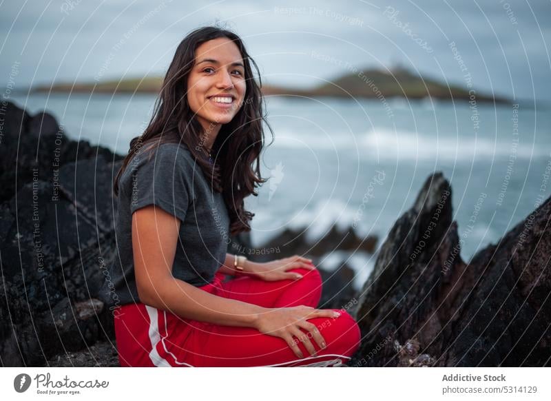 Young woman sitting on rock near ocean cliff sea coast mountain nature rocky foam shore ireland sky happy wave female cloudy young water positive admire