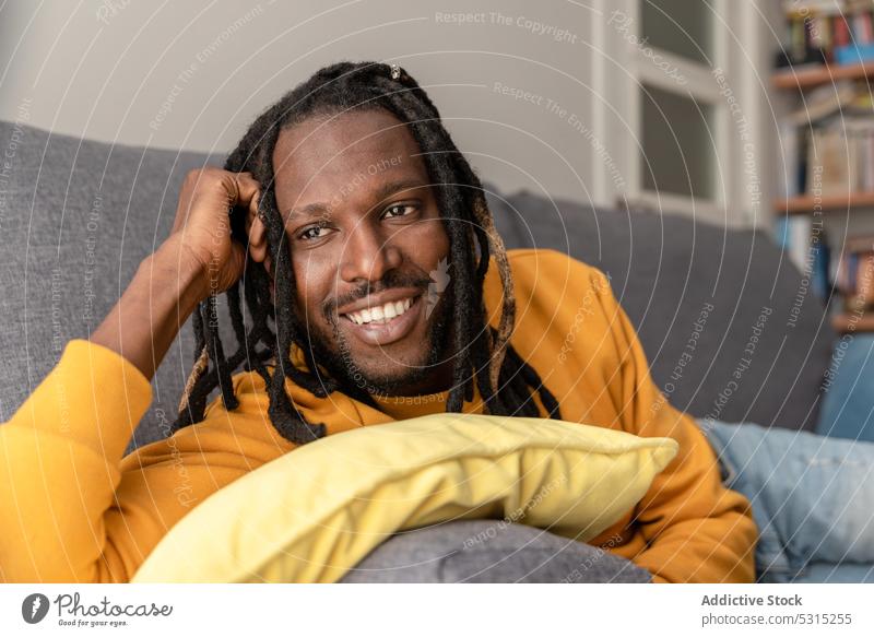 Cheerful black man lying on sofa with pillow smile positive home relax rest weekend cheerful hoodie male happy ethnic dreadlocks chill style bright couch joy