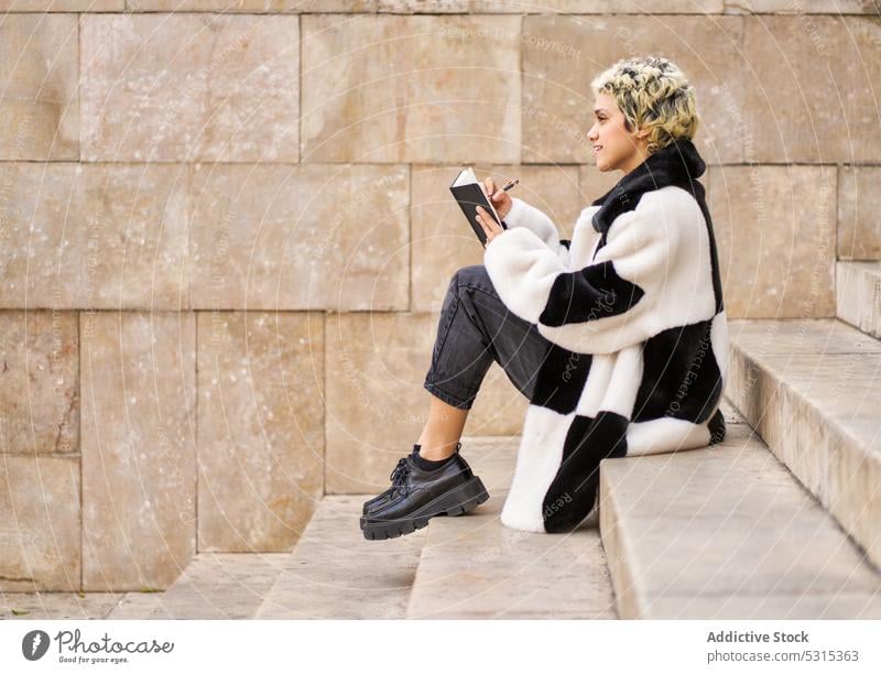 Cheerful woman taking notes on stairs take note notebook write student study smile positive young female planner education happy trendy step cheerful diary memo