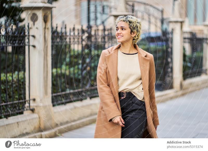 Cheerful woman in stylish outfit walking on pavement smile building street historic style city positive female blond trendy young architecture happy cheerful