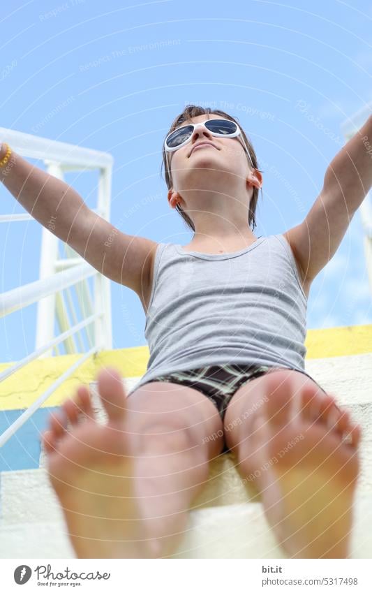 ¥Frog perspective l spaceship Enterheiß l young girl sits on stairs of slide, diving board, diving tower and looks up to the sky. Child with sunglasses sits on ladder in swimming pool and looks, looks up. Surrealism, surreal, retro.