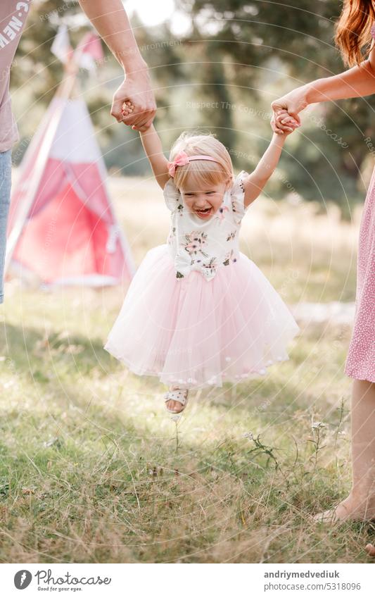 View on toddler. Mother, father hold hands daughter enjoy nature and walk in the park. Young family spending time together on vacation, outdoors. The concept of family summer holiday.