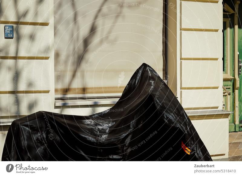 Shrouded two-wheeler under black tarpaulin in front of house facade of the founding period with shadow shrouded Black Facade Motorcycle Scooters Sheath cover