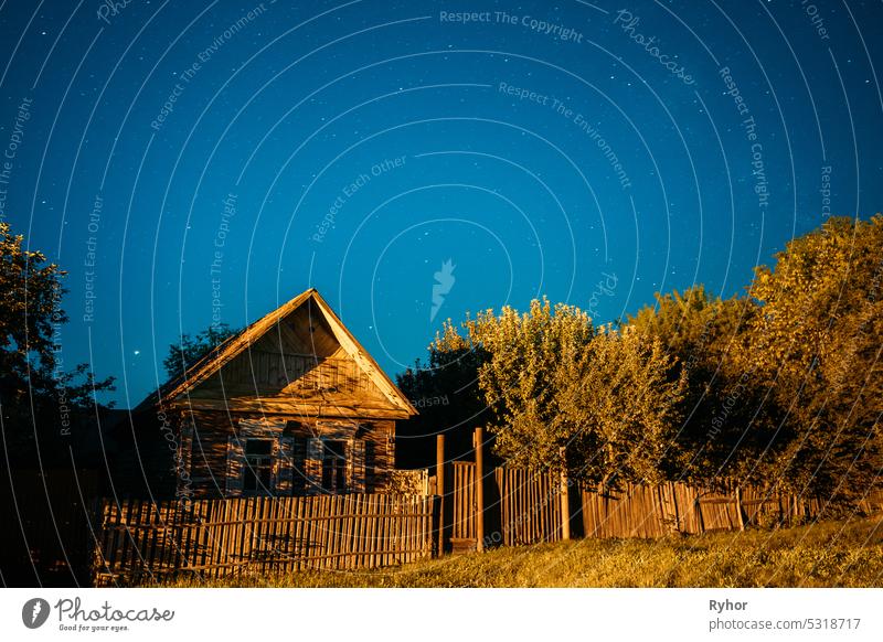 Night sky over old house in village. Night starry sky above house with bright stars and meteoric track trail. Glowing stars above summer nature reflection