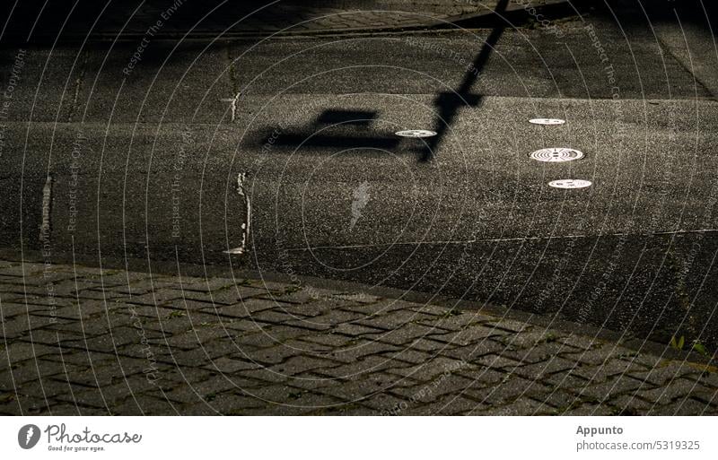 Asphalt surface of a street with paved sidewalk backlit with the shadow of a street sign Street Back-light Sun Shadow Surface Town urban road surface