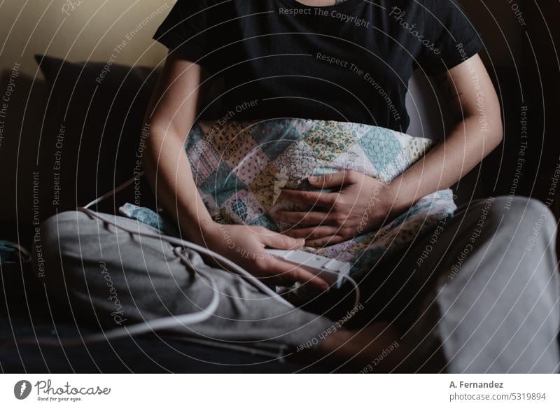 Detail of a woman using an electric blanket on her stomach area to relieve pain through heat therapy heated blanket bed warmer heater menstrual pain