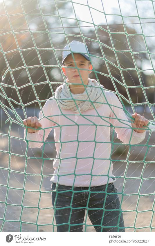 Portrait of teenager with cap behind a rope net in a park looking away. portrait male street young man boy youth lifestyle guy city photogenic urban student