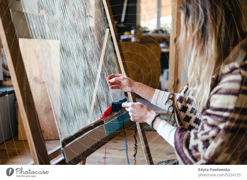 Crafty woman weaving at a loom at her workshop real people knitting machine wool yarn expertise garment making material spool entrepreneur craftsperson