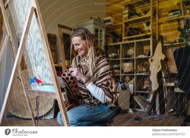 Crafty woman weaving at a loom at her workshop real people knitting machine wool yarn expertise garment making material spool entrepreneur craftsperson