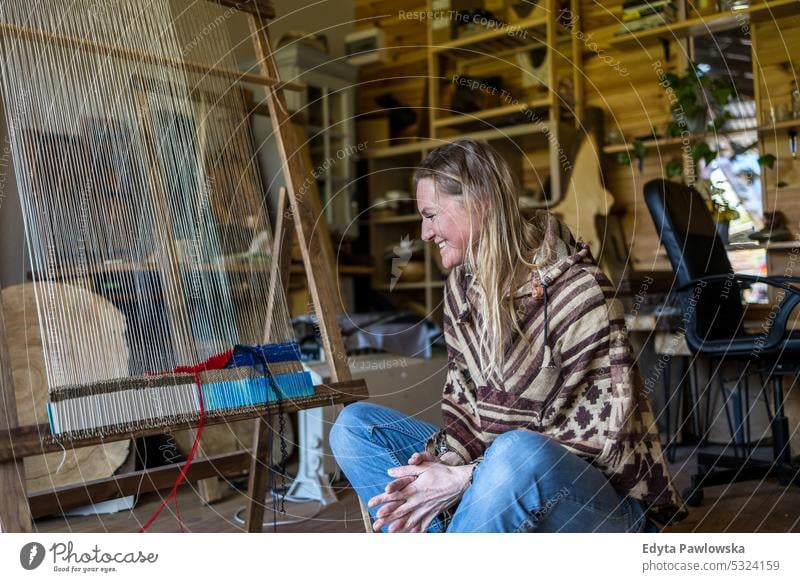 Crafty woman weaving at a loom at her workshop real people knitting machine wool yarn expertise garment making material spool entrepreneur craftsperson