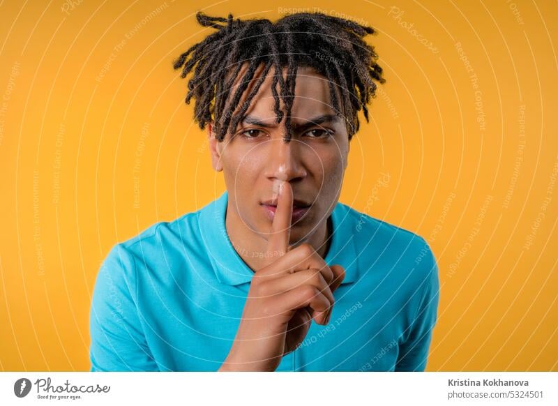 Handsome african man with gesture of shhh, secret, silence, conspiracy, gossip asking background biting charming closeup concept contemplation cute decision