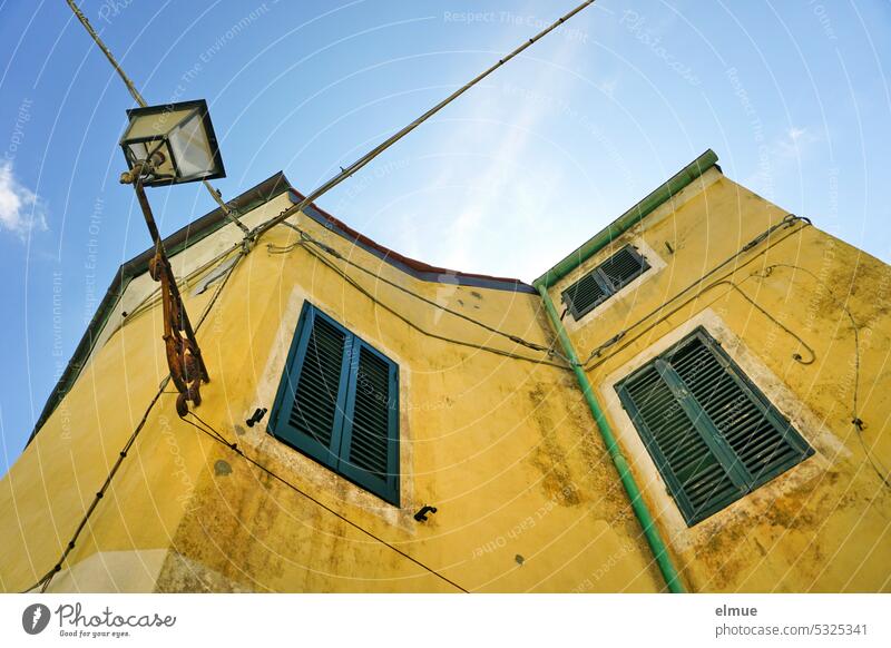 live on Elba - winding yellow apartment building with shutters in front of the windows and a street lamp from the frog perspective Apartment Building Poggio