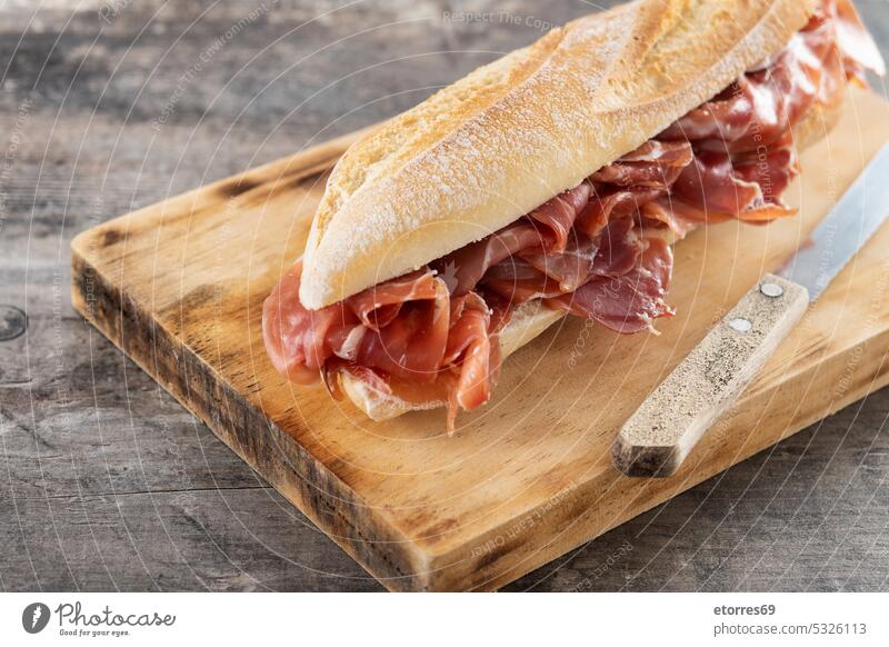 Spanish serrano ham sandwich on wooden table baguette bocadillo bread delicatessen delicious food gastronomy gourmet homemade iberian jamon meat mediterranean