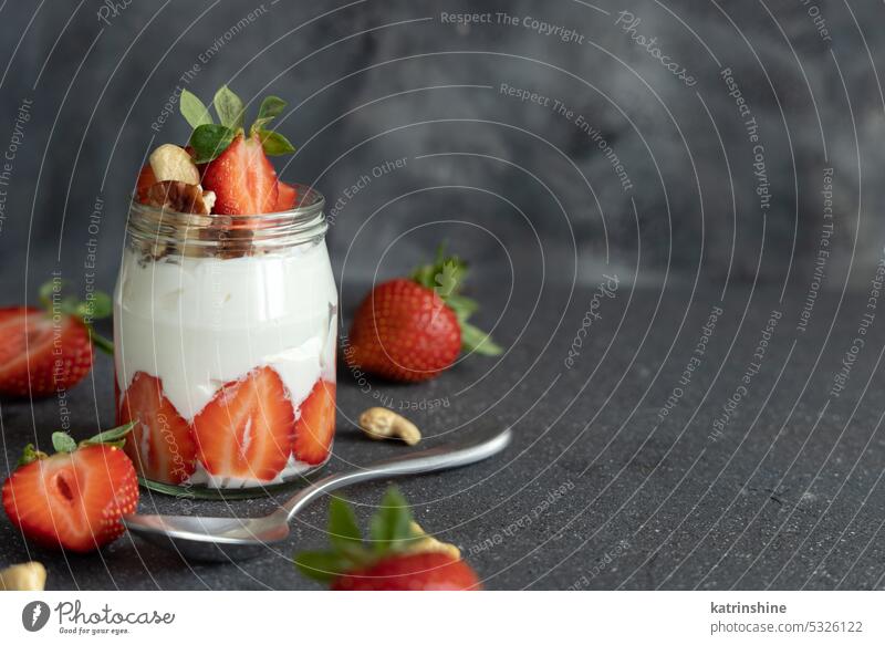 Greek yogurt, nuts and strawberries in a glass jar on grey table with a spoon close up, copy space breakfast Healthy fruits eat protein concrete red food