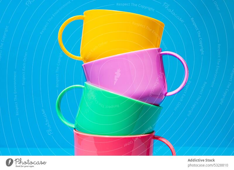 Multicolored ceramic cups on blue background saucer mug stack tower colorful bright composition shape table design porcelain dishware creative set minimal vivid