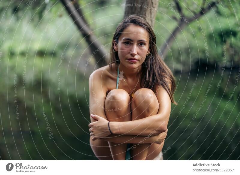 Calm woman embracing knees on tree trunk lake woods forest summer vacation nature relax water female young holiday bikini pond swimwear tranquil calm summertime