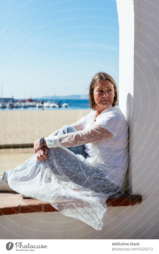 Woman sitting on windowsill viewing beach on sunny day woman sea rest border coast summer mature relax casual middle age shore female vacation ocean lifestyle