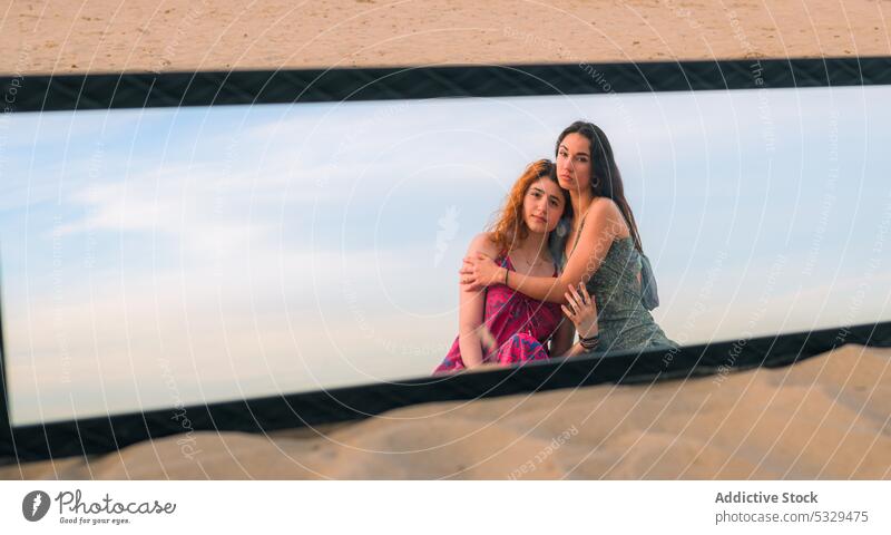 Calm women resting on sandy beach together mirror reflection hug friend summer pensive thoughtful friendship female young calm nature embrace peaceful coast