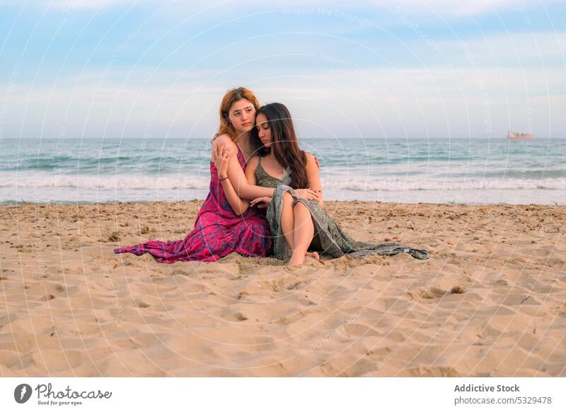 Pensive girlfriends sitting on sandy beach women thoughtful dreamy sea hug embrace tender summer ocean female shore pensive young resort wave friendship