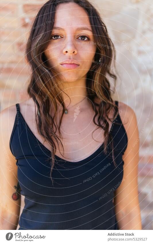 Calm woman in black top calm unemotional emotionless portrait appearance wavy hair attractive serene gaze personality brick wall serious female long hair