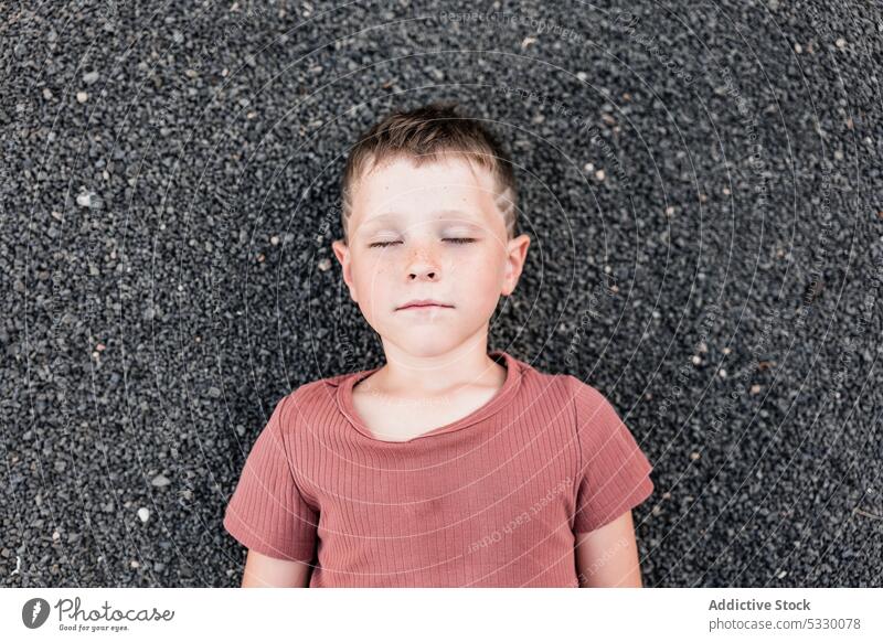 Pensive boy lying on stony shore with eyes closed summer dreamy thoughtful beach vacation pensive rest stone relax child nature calm seashore peaceful coast