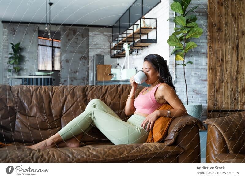 Relaxed woman drinking coffee on sofa in cozy room rest hot drink home comfort relax living room casual young cup lifestyle female couch tea chill asian ethnic