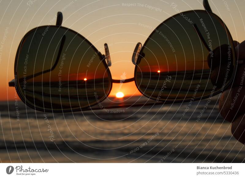 Sunglasses pointing to the sunset at the sea what looks like a face. Sunset Ocean Water Sunlight Sunbeam Exterior shot Landscape object Nature Beach Hand Face