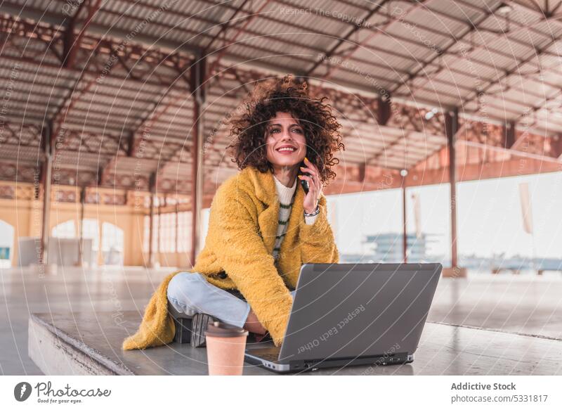 Smiling woman drinking coffee and speaking on smartphone on street laptop freelance phone call cafe remote work talk internet using female positive bench smile