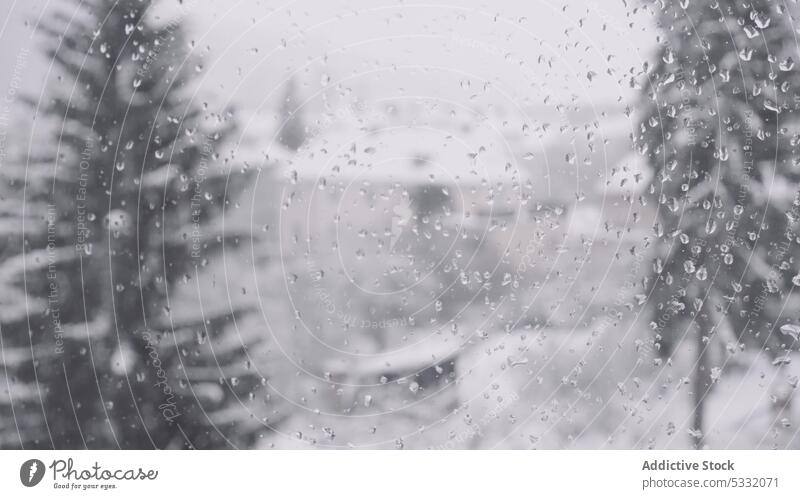 Glass with raindrops against blurred snowy street in winter town window condense glass transparent droplet pane wet wintry wintertime obscure translucent effect