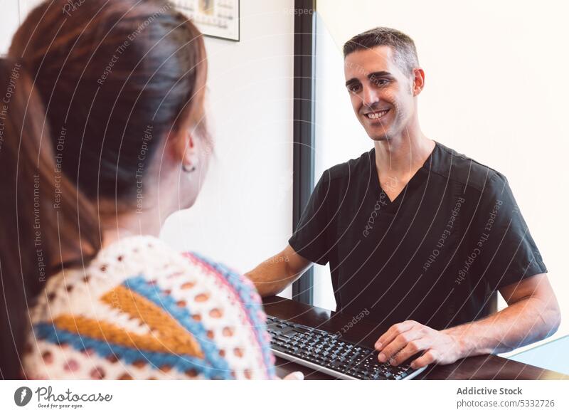 Cheerful doctor talking to patient in clinic woman discuss hospital computer work medicine speak conversation female positive health care explain visit smile