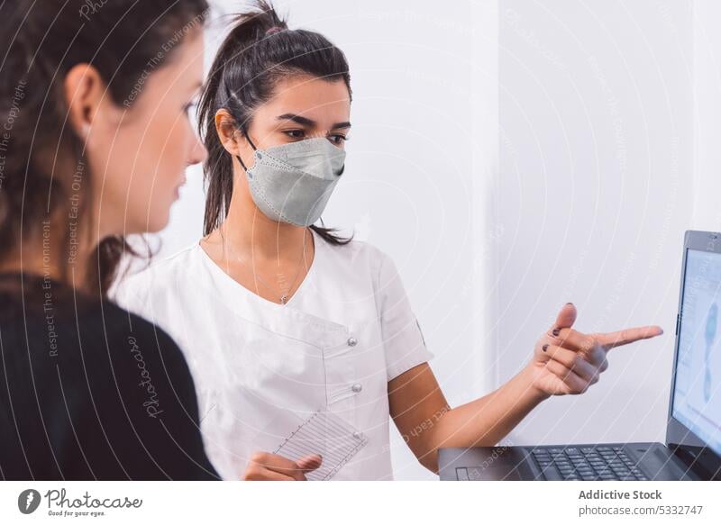 Focused doctor explaining problem to patient women laptop discuss mask clinic medical talk specialist hospital health care job uniform consult device treat