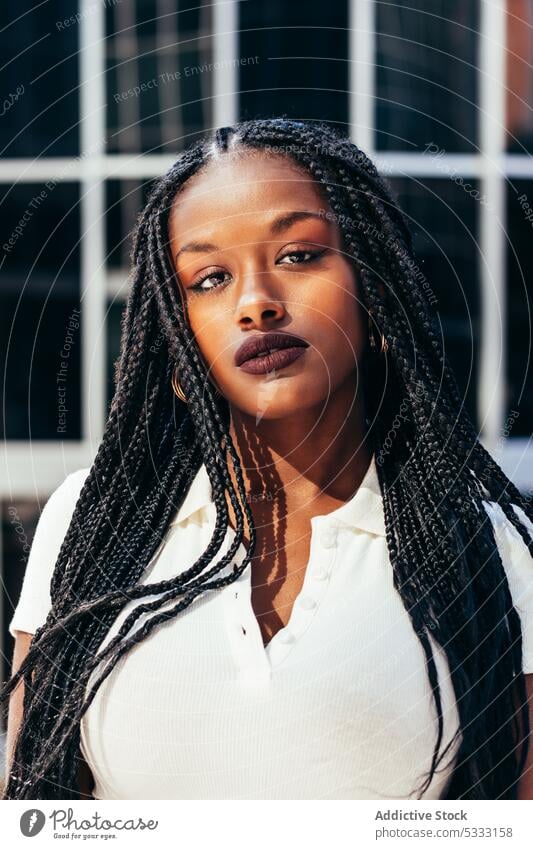 Black woman with long braided hair on street portrait stare urban trendy cool gaze emotionless individuality self assured afro braids style ethnic female young