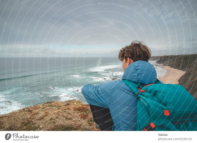 Young man sits above the famous Praia da Carreagem beach in southwest Portugal, near the town of Aljezur in the Odemira region. Wandering along the Fisherman Trail