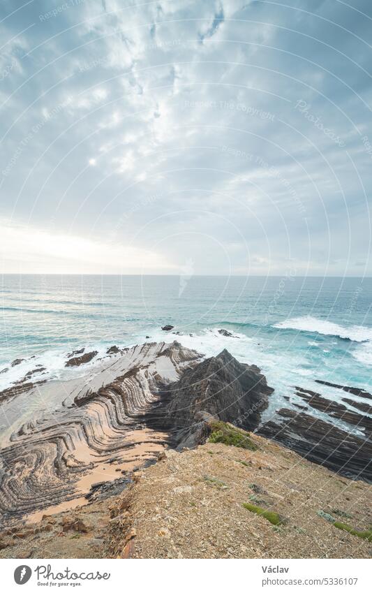 Rocky cliffs with futuristic patterns on the Atlantic coast near the town of Aljezur in southwestern Portugal. The sound of the ocean as the sun sets. Wandering the Rota Vicentina