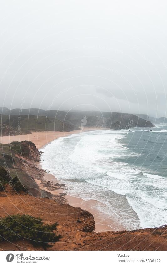 Portugal's western coastline of rocky cliffs and sandy beaches in the Odemira region. Wandering along the Fisherman trail on rainy days splash stormy weather